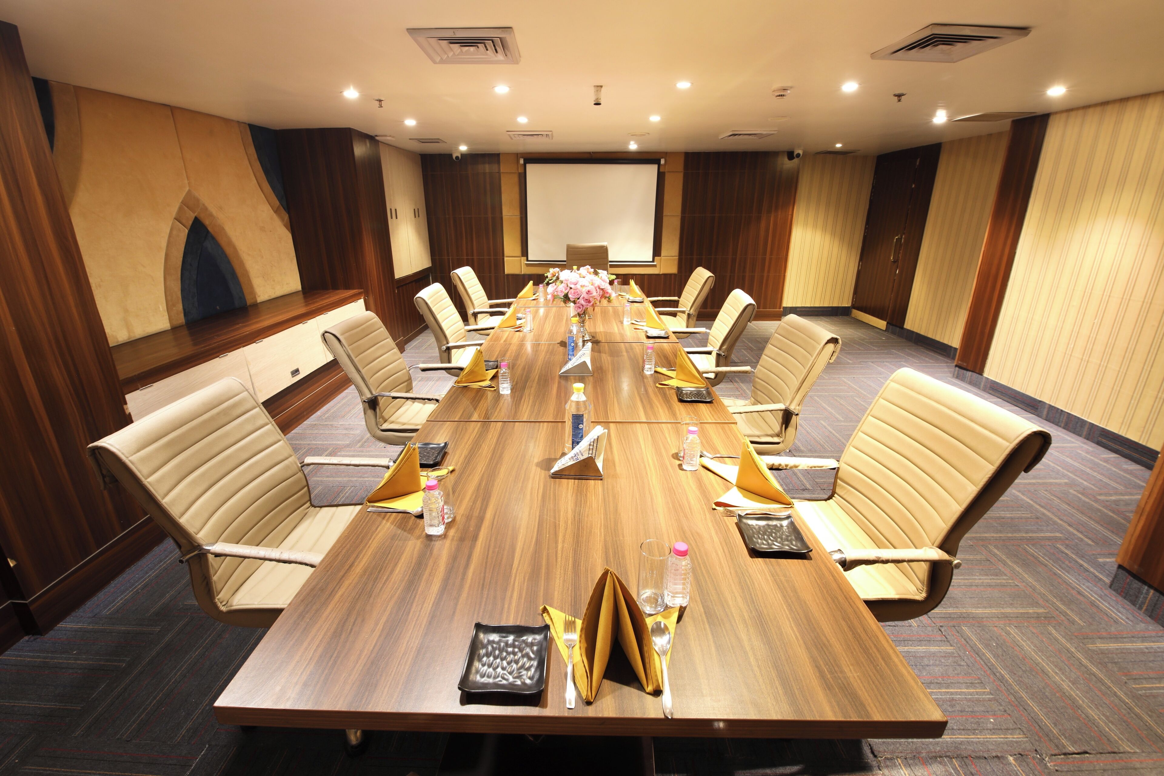 Un salón de conferencias con una larga mesa, varias sillas y una pantalla para proyector.