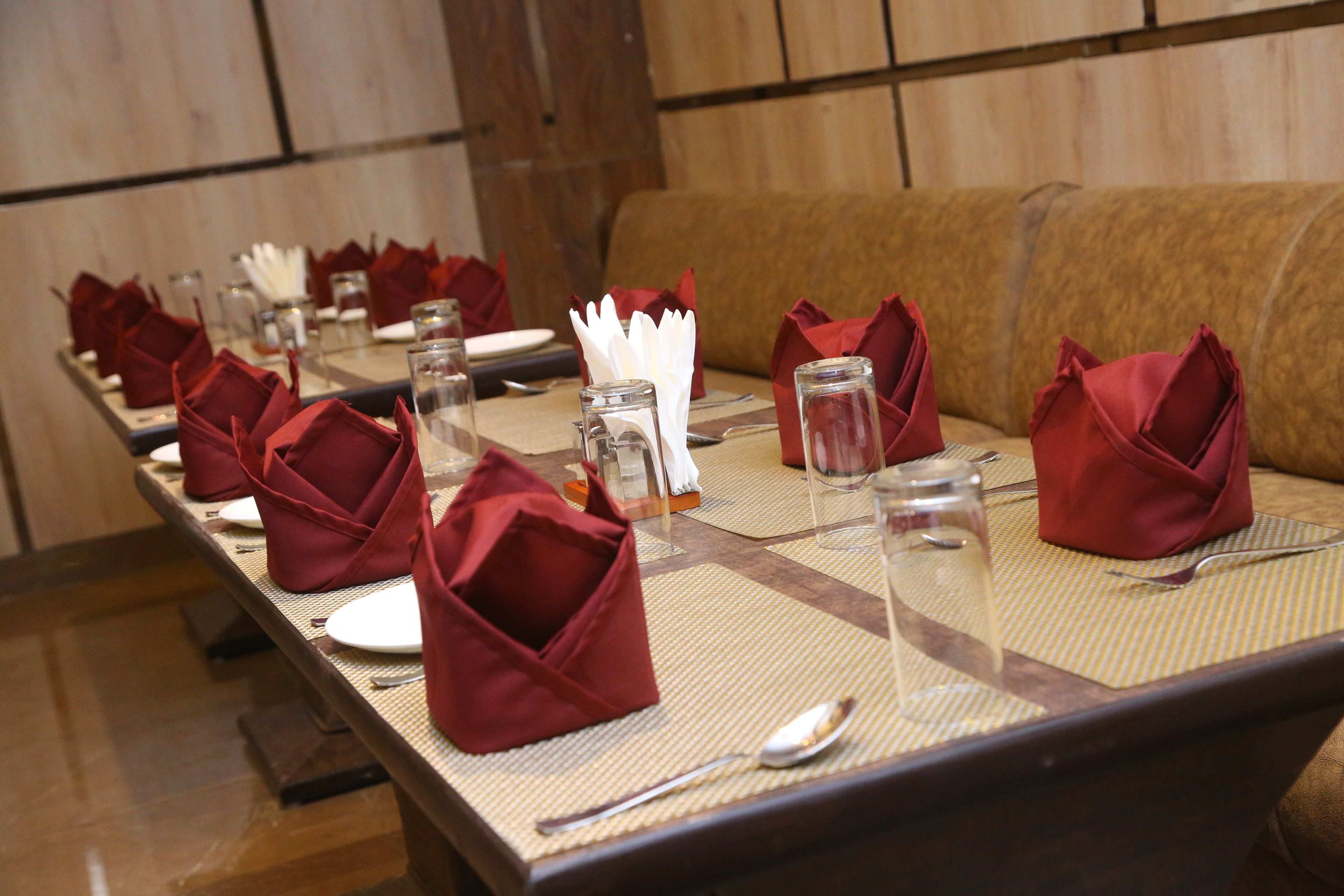 Une longue table à manger, dressée avec des serviettes rouges, de la vaisselle transparente et des couverts en argent.