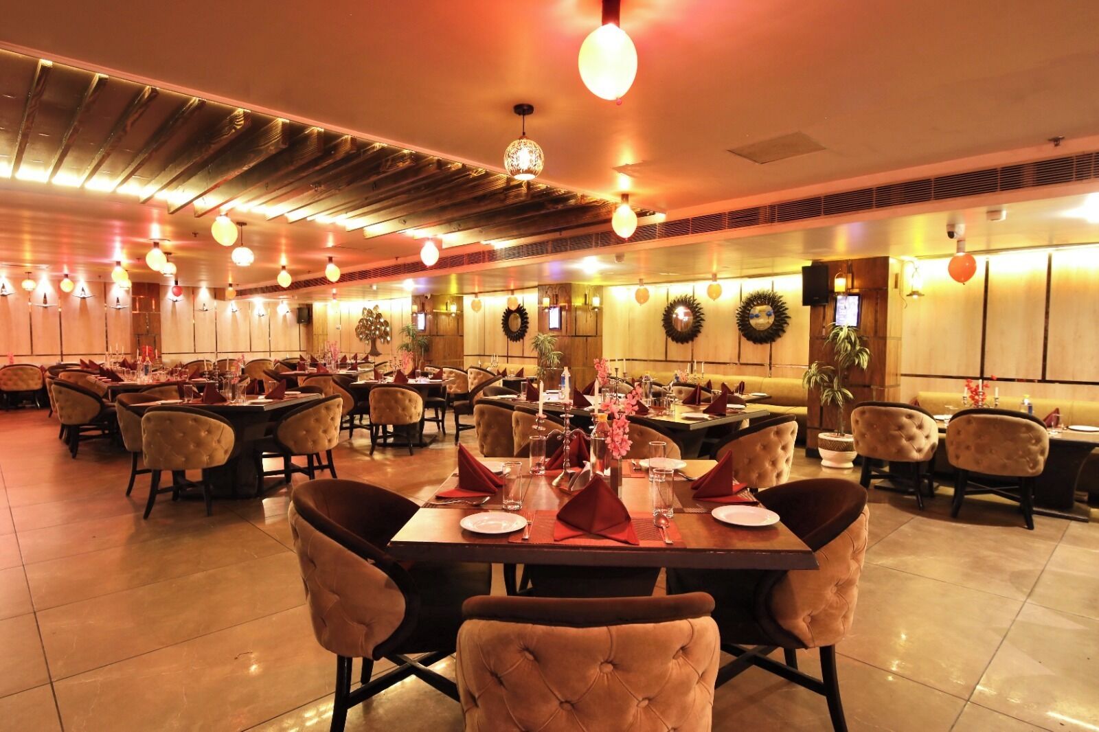 A spacious restaurant with multiple dining tables and chairs, warm lighting, and decorative wall elements.