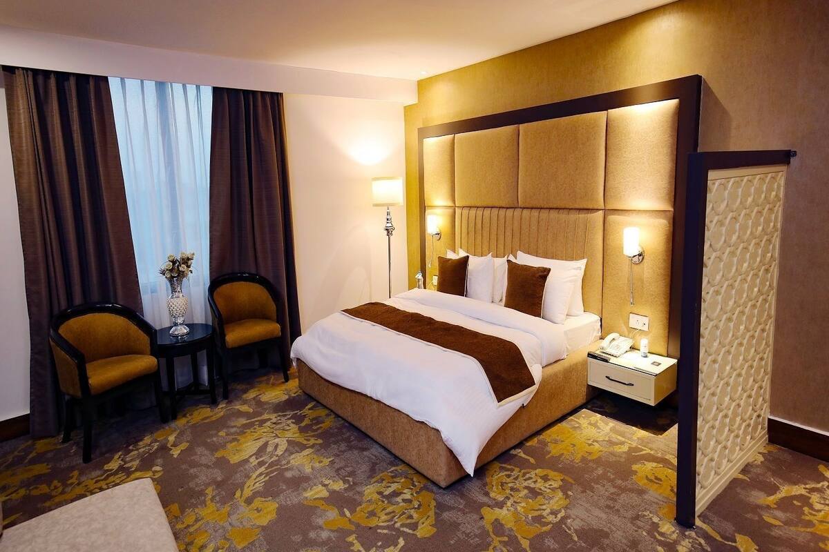 A hotel room with a large bed, two armchairs, a small table, a nightstand with a phone, and a decorative vase.