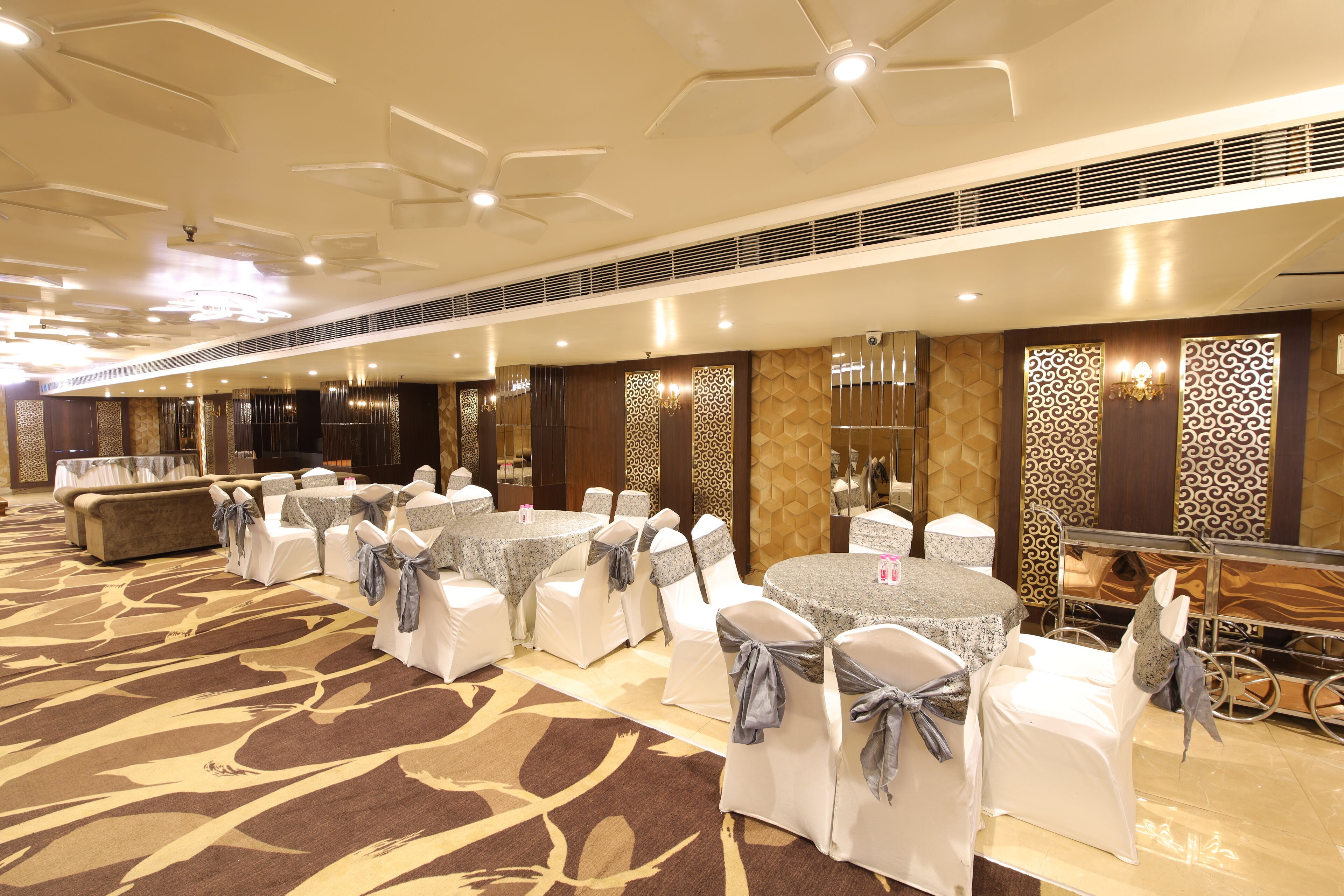 A banquet hall with round tables and white chairs, some with gray sashes.