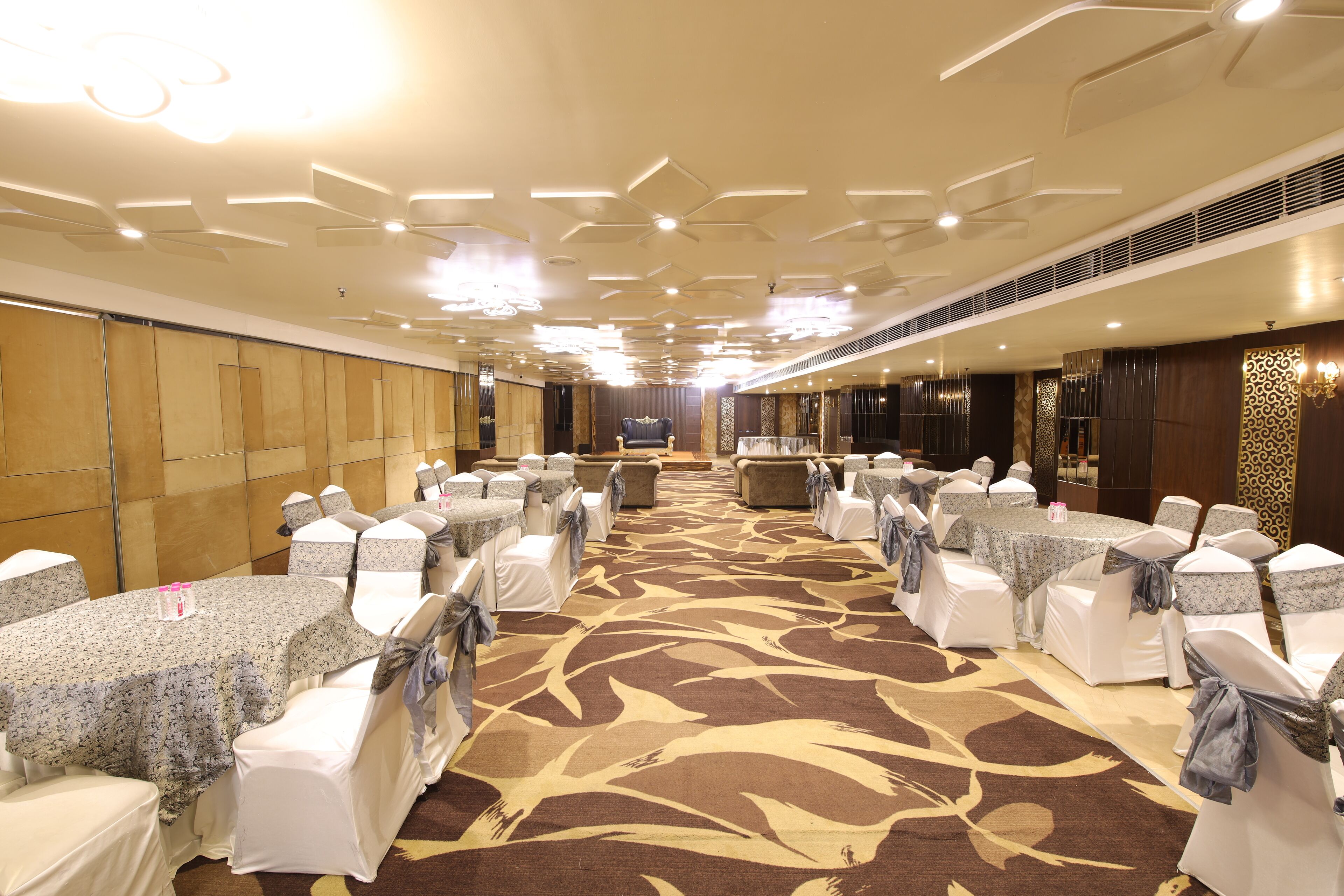 A banquet hall with rows of tables and chairs, a patterned carpet, and a modern ceiling design.