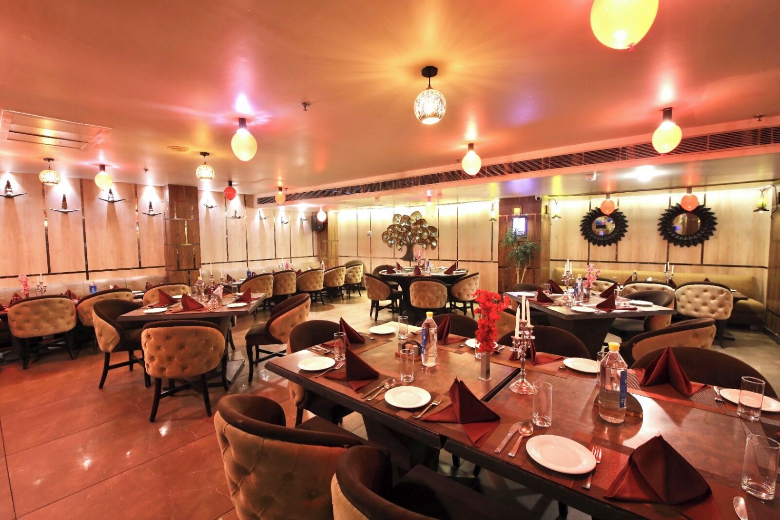 Un restaurant avec des tables rondes, des chaises rembourrées et des luminaires suspendus.