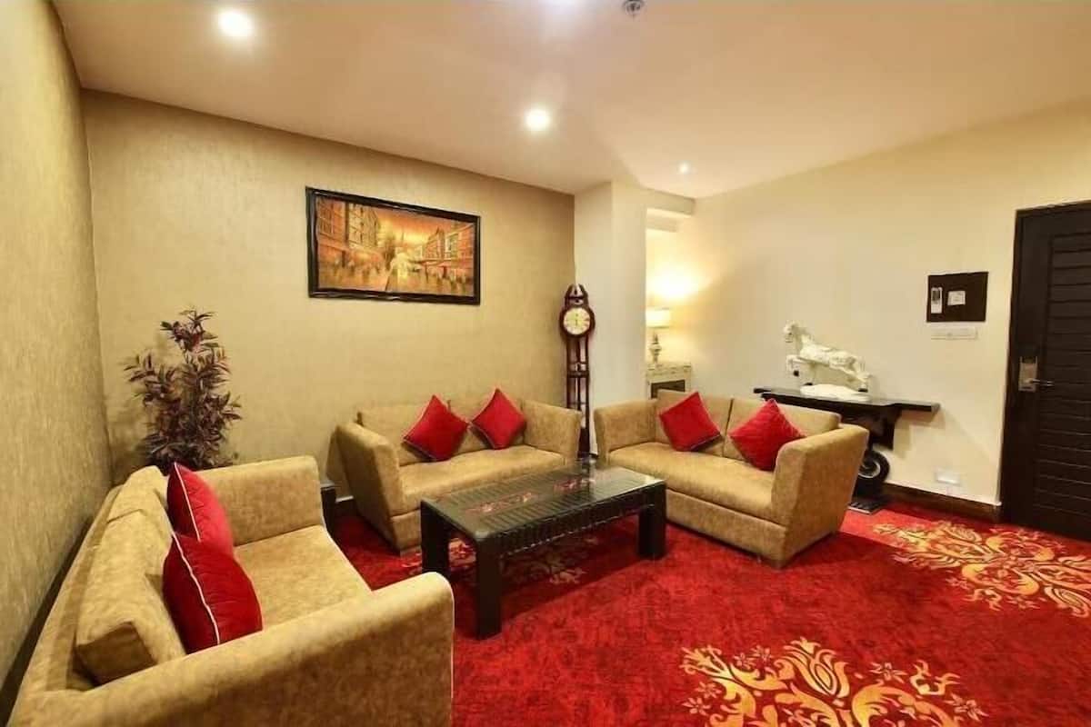 A hotel room with beige sofas, red cushions, a wooden coffee table, a red carpet, a wall-mounted clock, a framed picture, a statue, and a door with a sign.