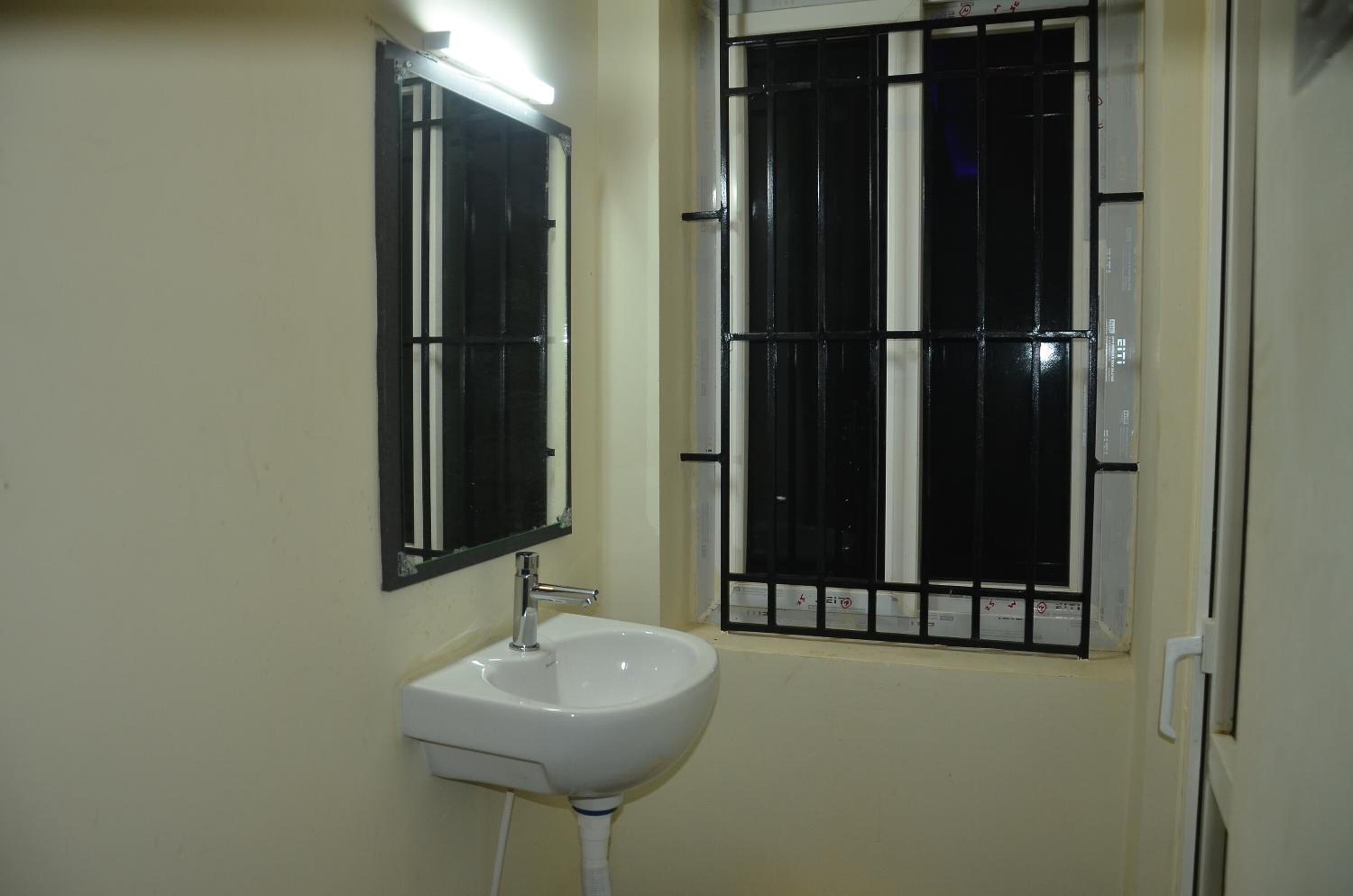 A bathroom with a white sink, a mirror, and a window with black bars.