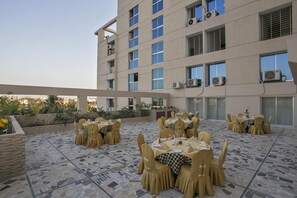 A rooftop dining area with multiple tables and chairs, air conditioning units, and a view of the cityscape. - Hotel Nirvana Inn (Sylhet)