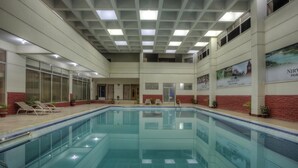En inomhuspool med klart vatten, omgiven av solstolar och krukväxter.