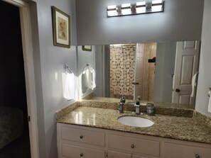 Un baño con lavamanos de encimera de granito, un espejo grande y un perchero para toallas.