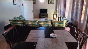 A living room with a sofa set, a dining table, chairs, a TV, and a window with curtains. - PENTHOUSE VIEW AND FLATS VACATION HOME (#2) (MONTEGO BAY)