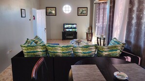 A living room with a TV, a dining table, and a sofa with patterned cushions. - PENTHOUSE VIEW AND FLATS VACATION HOME (#2) (MONTEGO BAY)