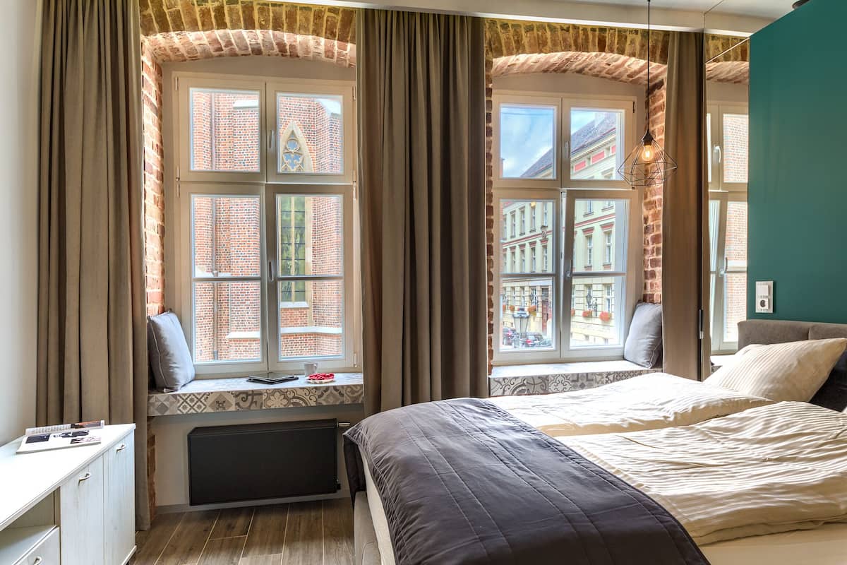 A bedroom with a large bed, a window seat with a view of a brick building, and a radiator under the window.