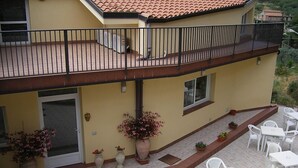 A two-story building with a balcony, outdoor seating area, and potted plants.