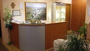 A reception area with a wooden counter, a large framed landscape painting, a cross, and a mirror above the counter.
