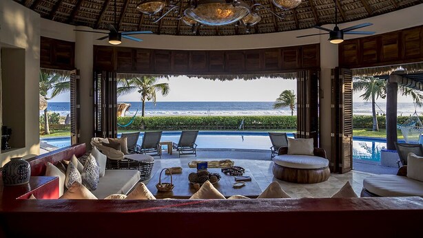 Un salon luxueux avec vue sur l’océan, doté d’un toit de chaume, de sièges confortables et situé au bord de la piscine.