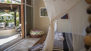 Une chambre à coucher avec un lit à baldaquin, un banc, un coin salon confortable et une vue sur l’extérieur.