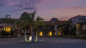 Un complexe hôtelier doté d’une cour, de palmiers et offrant une vue sur un ciel au coucher du soleil.