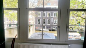 Une pièce avec vue sur un canal et des bâtiments, visible à travers une fenêtre à quatre carreaux.