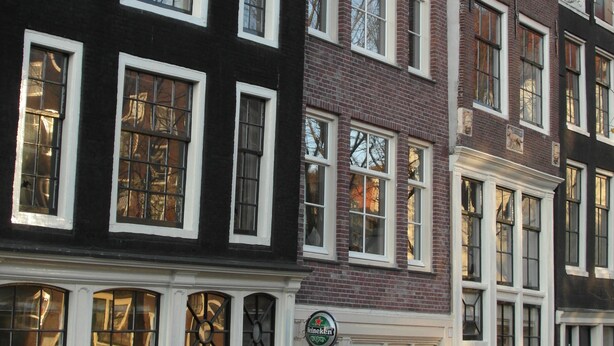 Une rangée de bâtiments européens traditionnels, caractérisés par une architecture uniforme au niveau des fenêtres et par une enseigne Heineken bien visible au rez-de-chaussée.