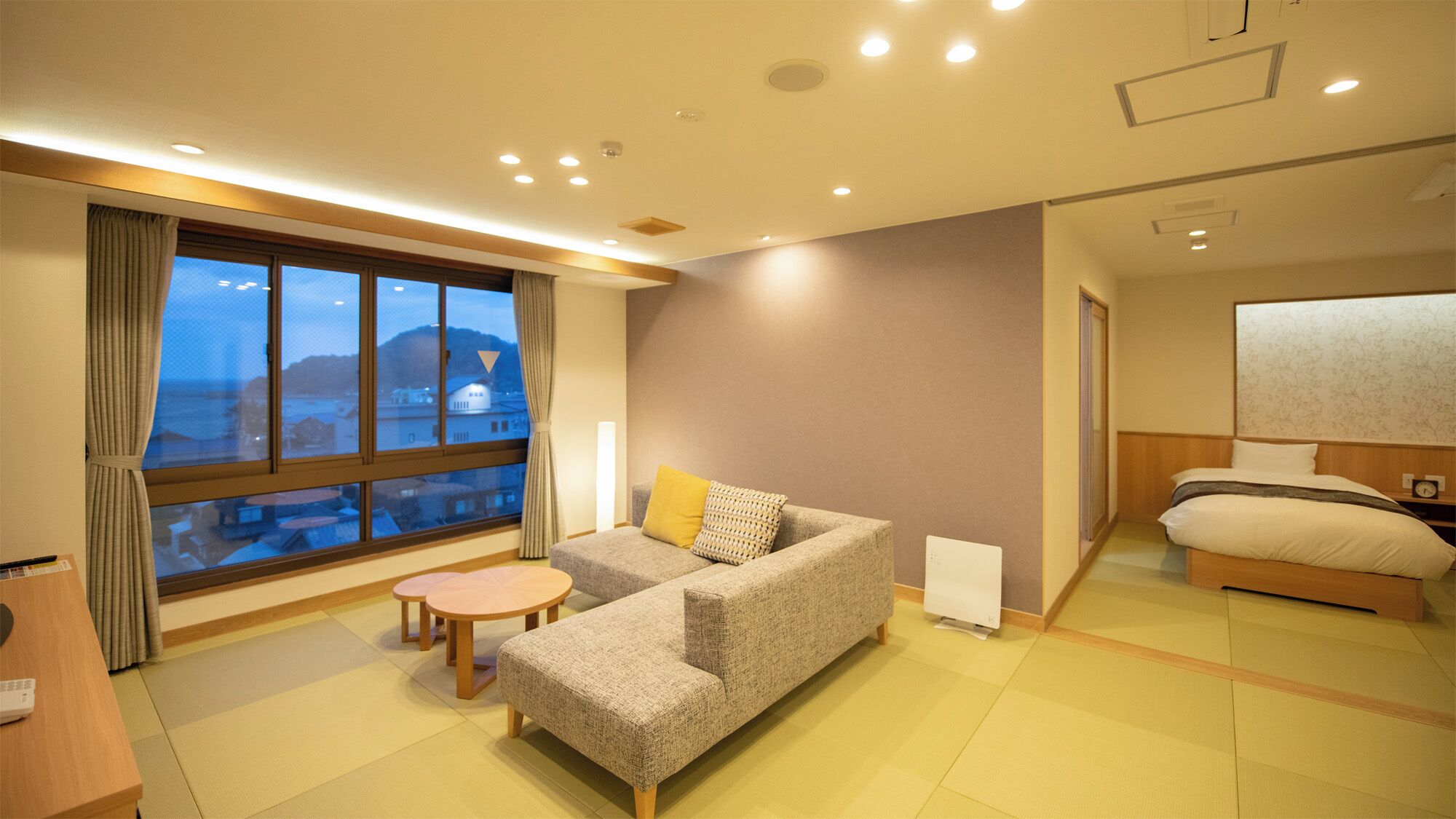 Una habitación de hotel con sofá, una mesita, cama y un gran ventanal con vistas al mar.