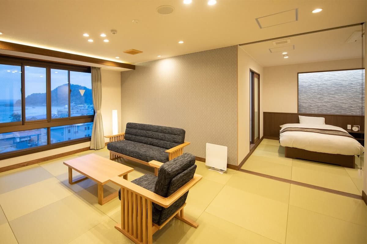 A hotel room with a sofa, a bed, a desk, and a view of the sea.