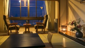 A traditional Japanese room with tatami flooring, a low table, two chairs, a large window with curtains, and a vase with flowers. - Kaisyu (Kyotango)