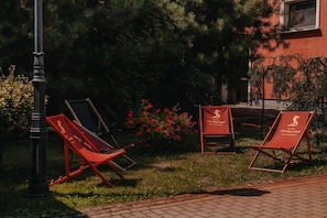 Un jardín con tres sillones rojos, un farol negro y un edificio de fachada roja.
