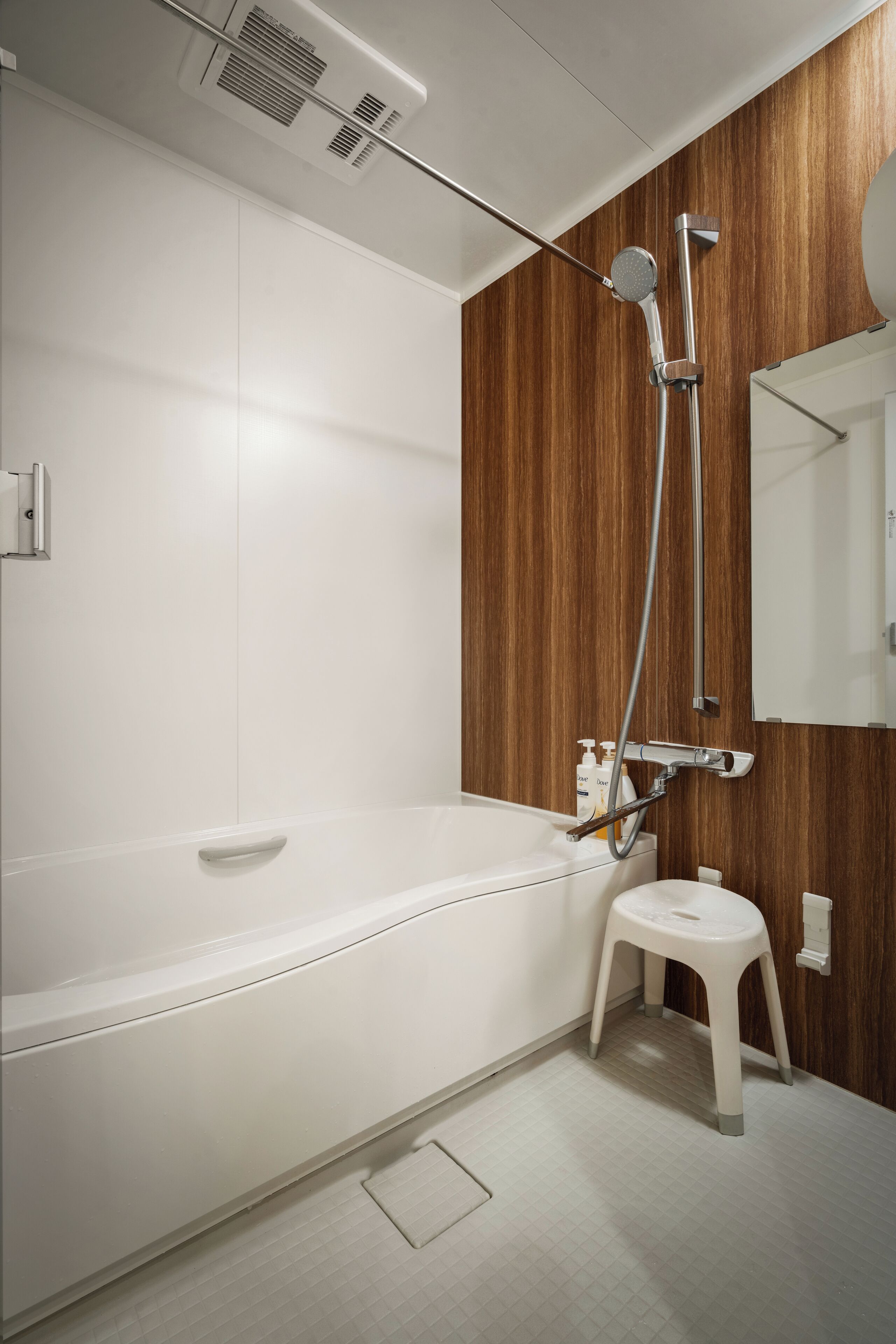 A modern bathroom with a white bathtub, a wooden accent wall, a shower with a handheld showerhead, and a small stool.