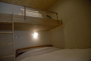 Una cama litera con estructura de madera, una mesita de noche pequeña y una luz fijada a la pared.