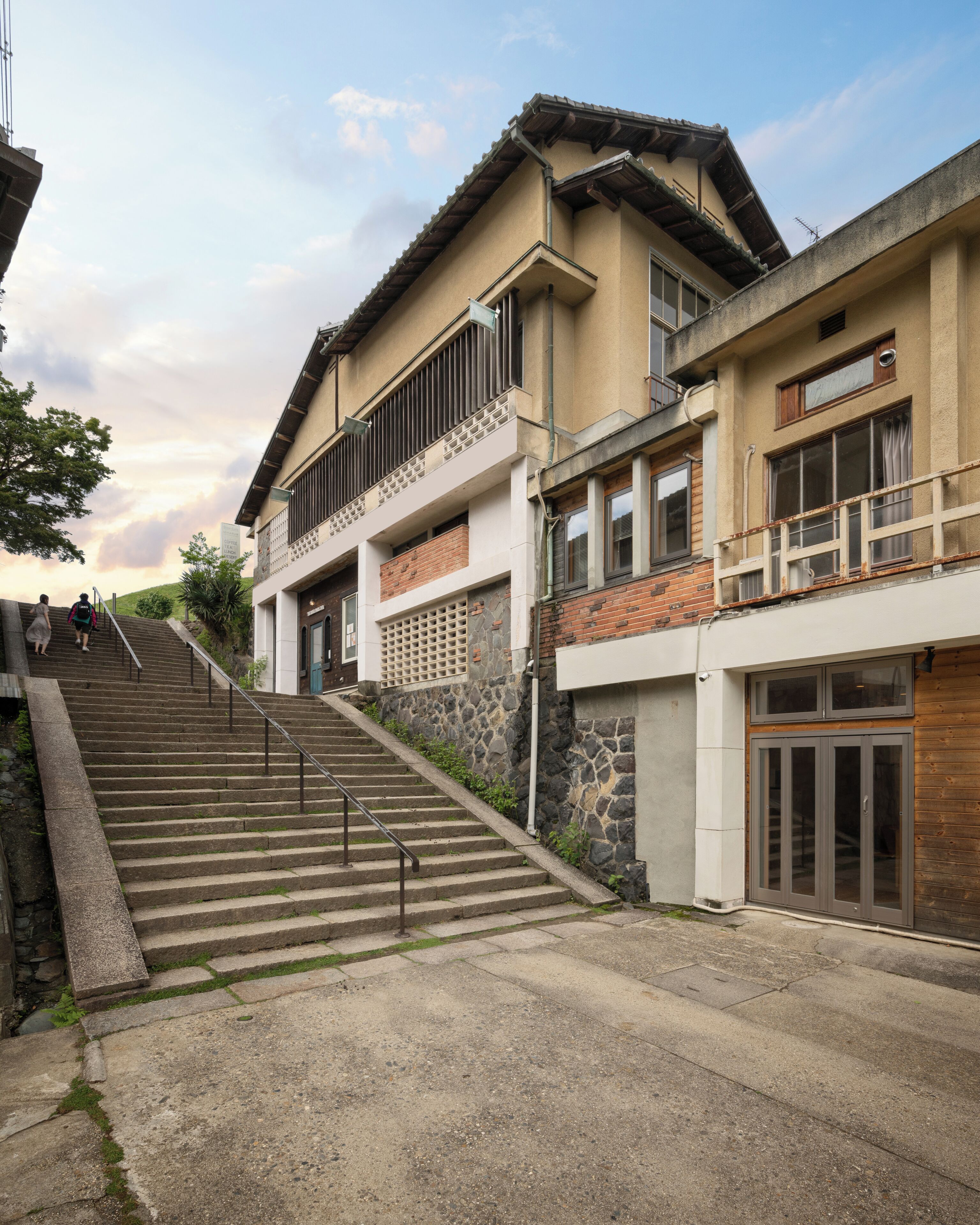Un edificio con una escalera que lleva a un balcón en el segundo piso, un muro de piedra y una puerta de madera.
