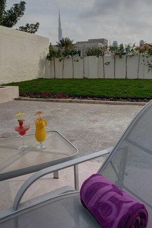 A glass table with two drinks and a purple towel on a balcony overlooking a cityscape with a prominent skyscraper.