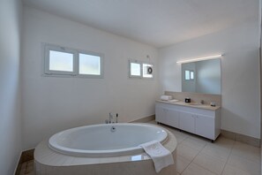 A modern bathroom with a freestanding bathtub, a vanity with a mirror, and two windows.