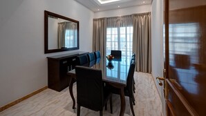 A modern hotel room with a dining area featuring a glass table, dark wooden chairs, and a large mirror. - J5 Four Bedroom Villa in Mirdif (Dubai)
