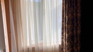 Une pièce dotée d’une grande fenêtre ornée de rideaux blancs et vaporeux, et d’un rideau à motifs sur le côté droit.