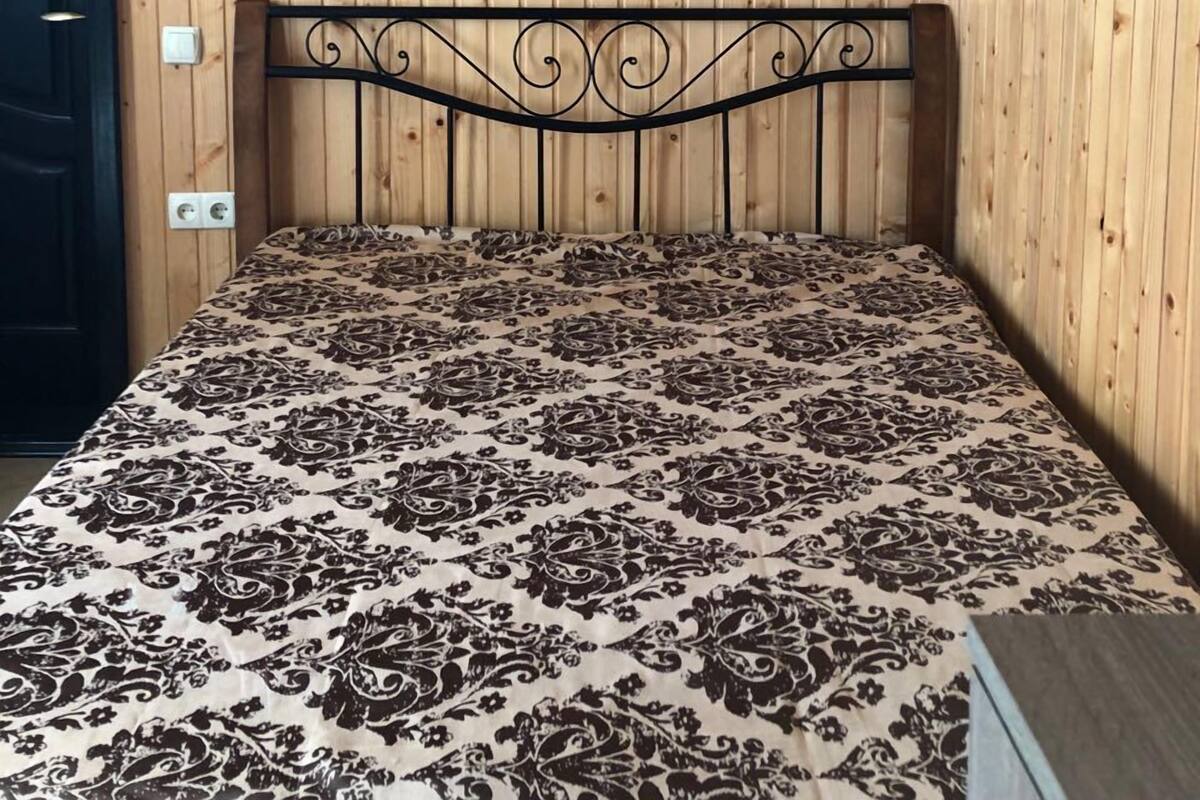 A room with a bed, wooden walls, an air conditioner, two wall-mounted lamps, and a door.