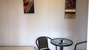 Une chambre d’hôtel comprenant un lit, deux chaises, une petite table ronde et deux œuvres d’art accrochées au mur.