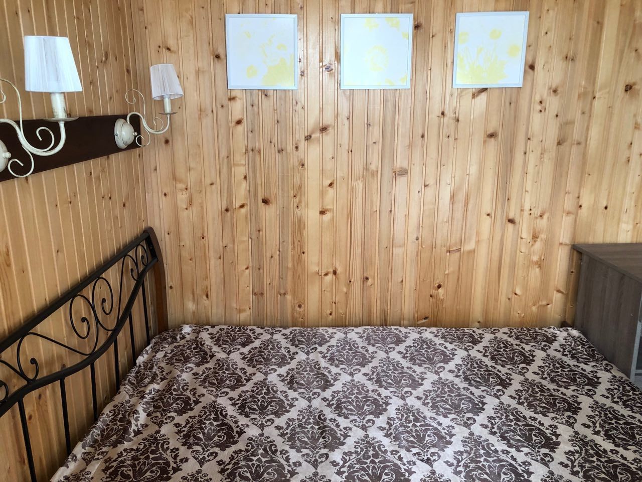 A wooden-paneled room with a bed, two wall-mounted lamps, and three framed pictures.