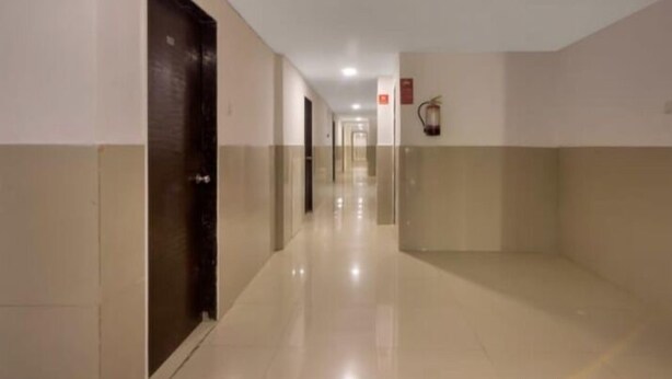 Un pasillo con puertas a ambos lados, un extintor en la pared derecha y una lámpara en el techo.