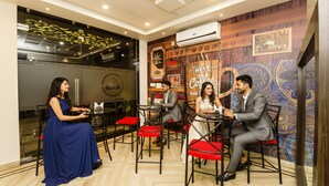 A cafe with four people seated at tables, featuring a modern interior with wooden accents and a mural. - FabHotel De Sivalika (Howrah)