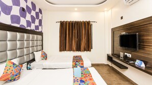 A hotel room with a large bed, a TV, a flat-screen TV mounted on the wall, and a window with curtains. - FabHotel De Sivalika (Howrah)