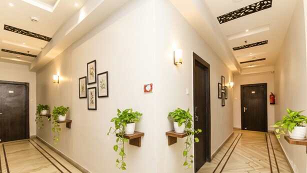 A hallway with marble flooring, framed botanical prints on the walls, and potted plants on shelves. - FabHotel De Sivalika (Howrah)