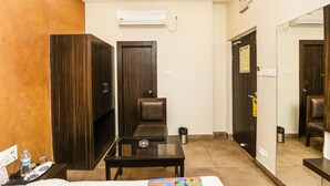 A hotel room with a bed, a small table, a chair, a wardrobe, and a trash bin. - FabHotel De Sivalika (Howrah)