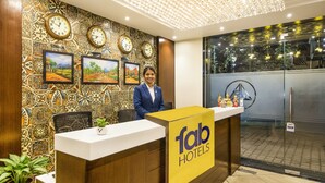 A hotel reception desk with a 'Fab Hotels' sign, multiple wall clocks, framed landscape paintings, and a modern chandelier. - FabHotel De Sivalika (Howrah)