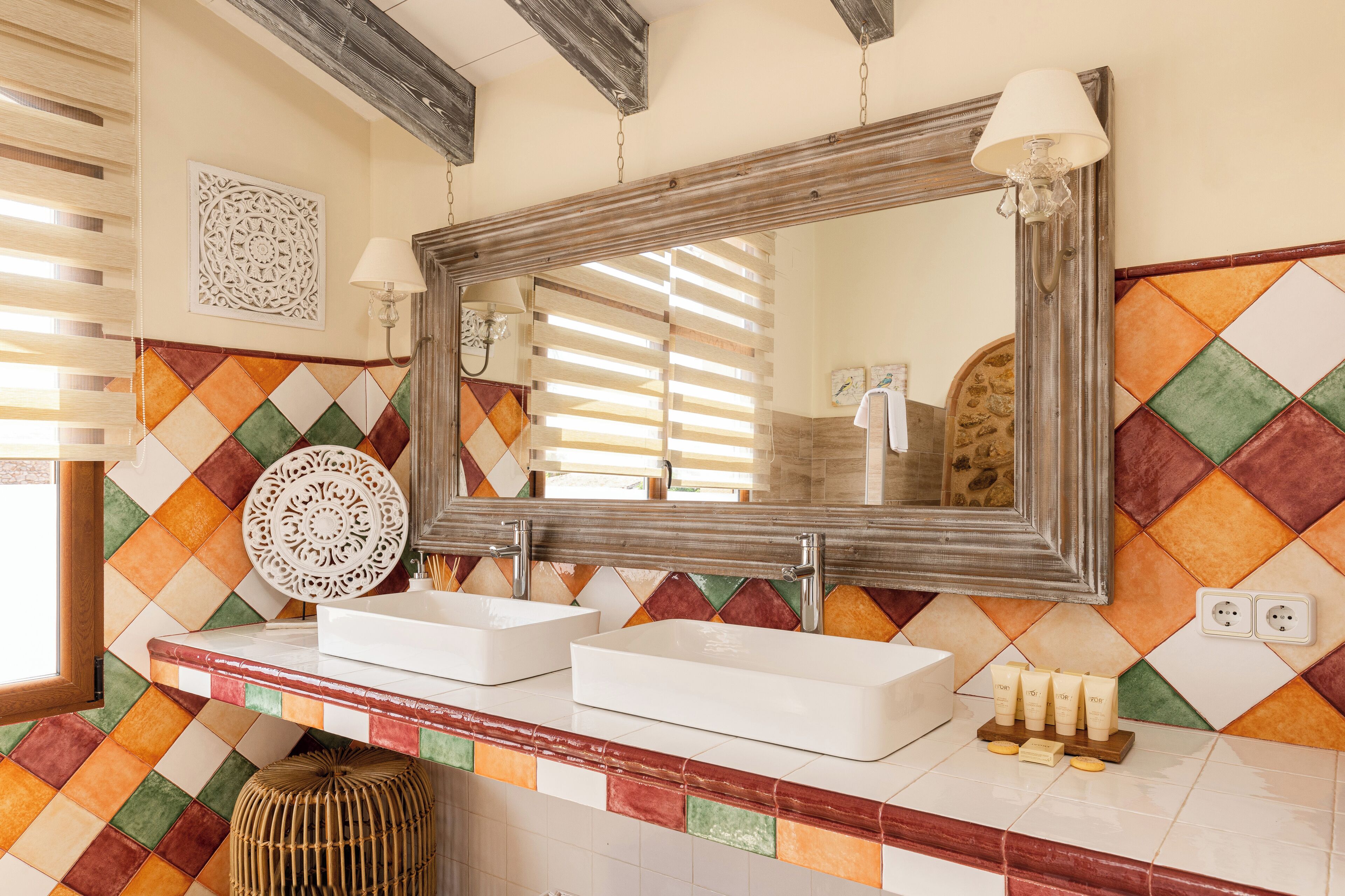 Un baño con dos lavamanos, un espejo y un colorido revestimiento de azulejos.