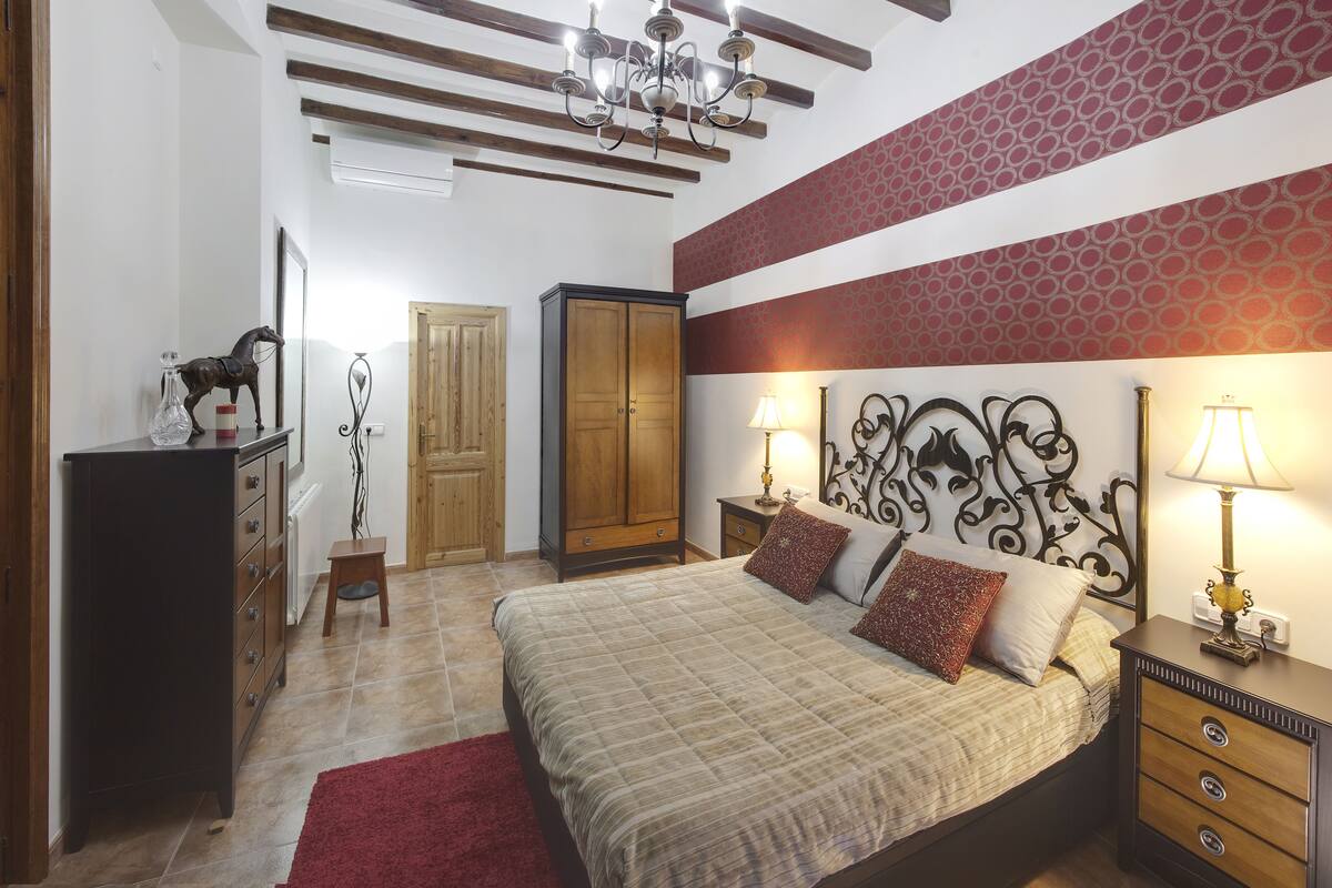 A bedroom with a bed, nightstands, a dresser, a chandelier, and a patterned wall.