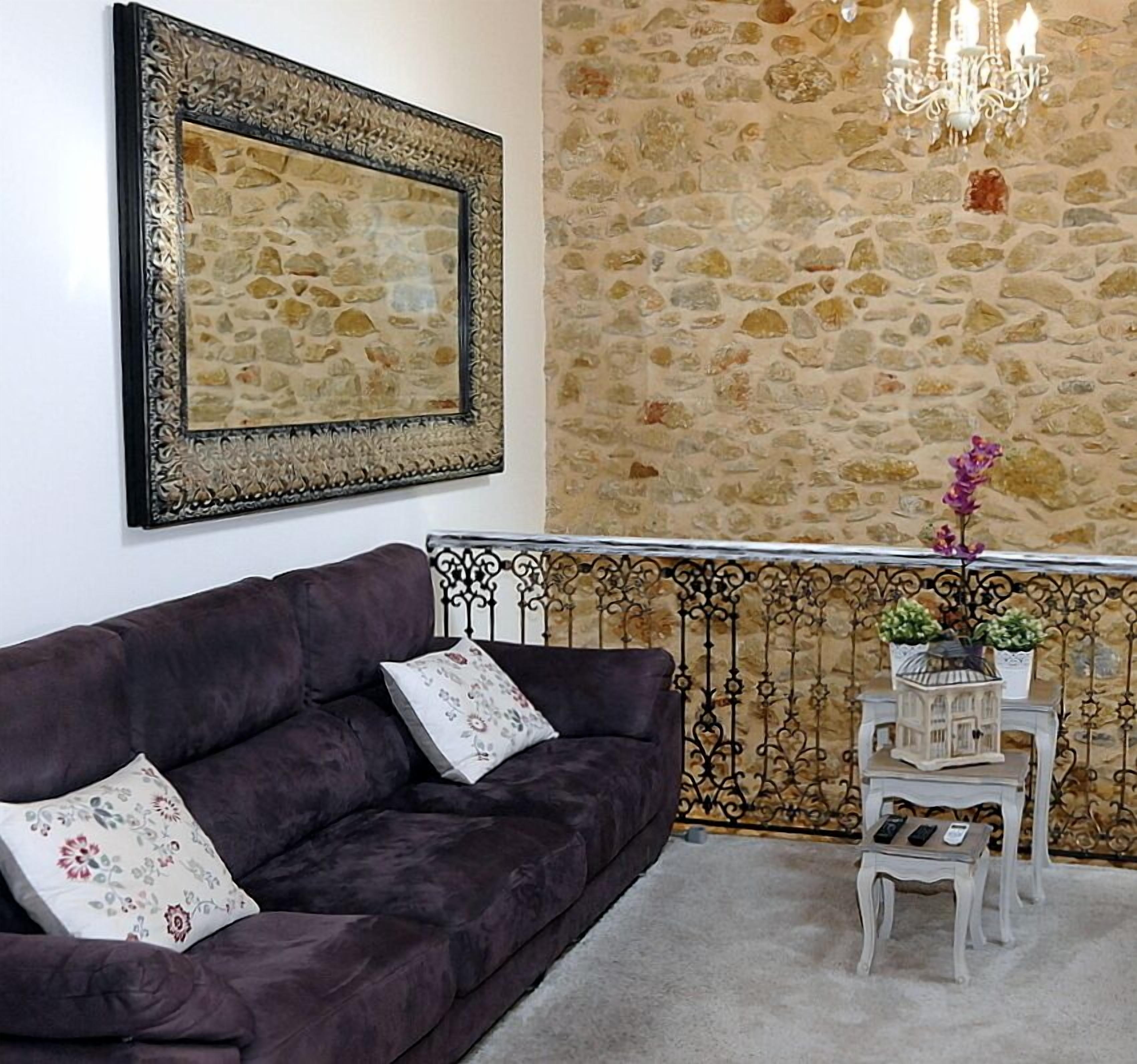 Una sala de estar con pared de piedra, un sofá color morado oscuro, una araña y una mesita con adornos.