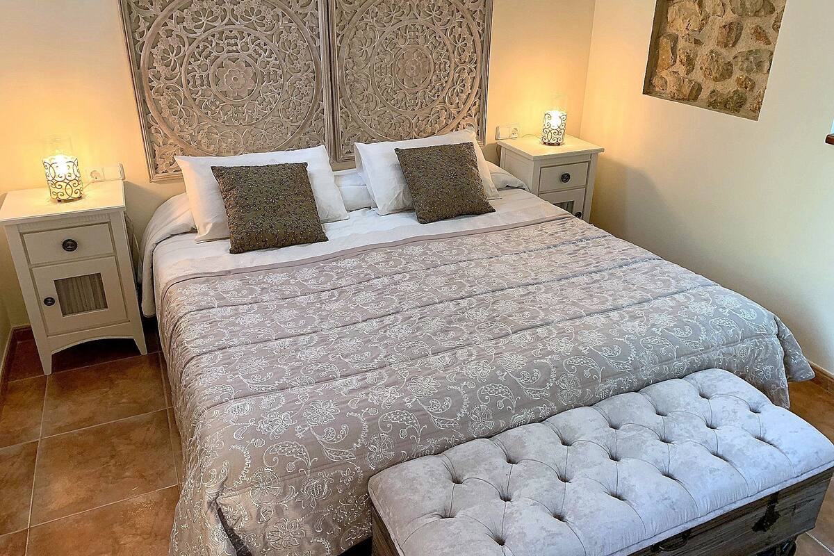 A bedroom with a large bed, two bedside tables, a nightstand, and a decorative headboard.