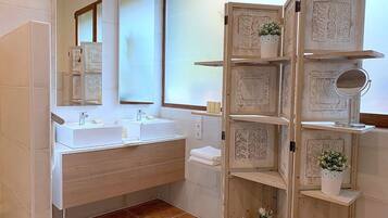 Un baño con tocador de madera, dos lavamanos, un espejo y estantes con objetos decorativos.