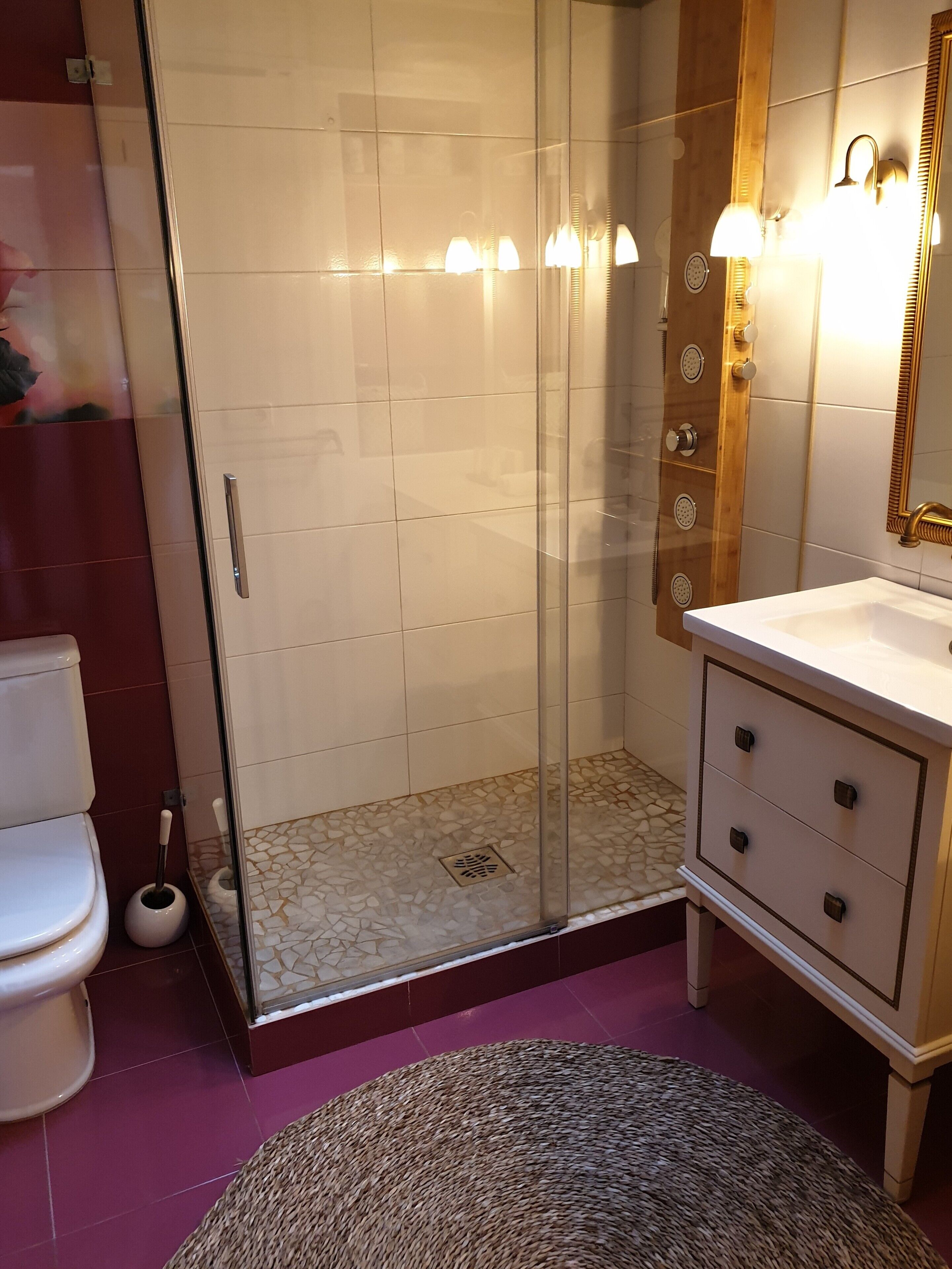 A bathroom with a glass-enclosed shower, a white sink with a wooden vanity, and a toilet.