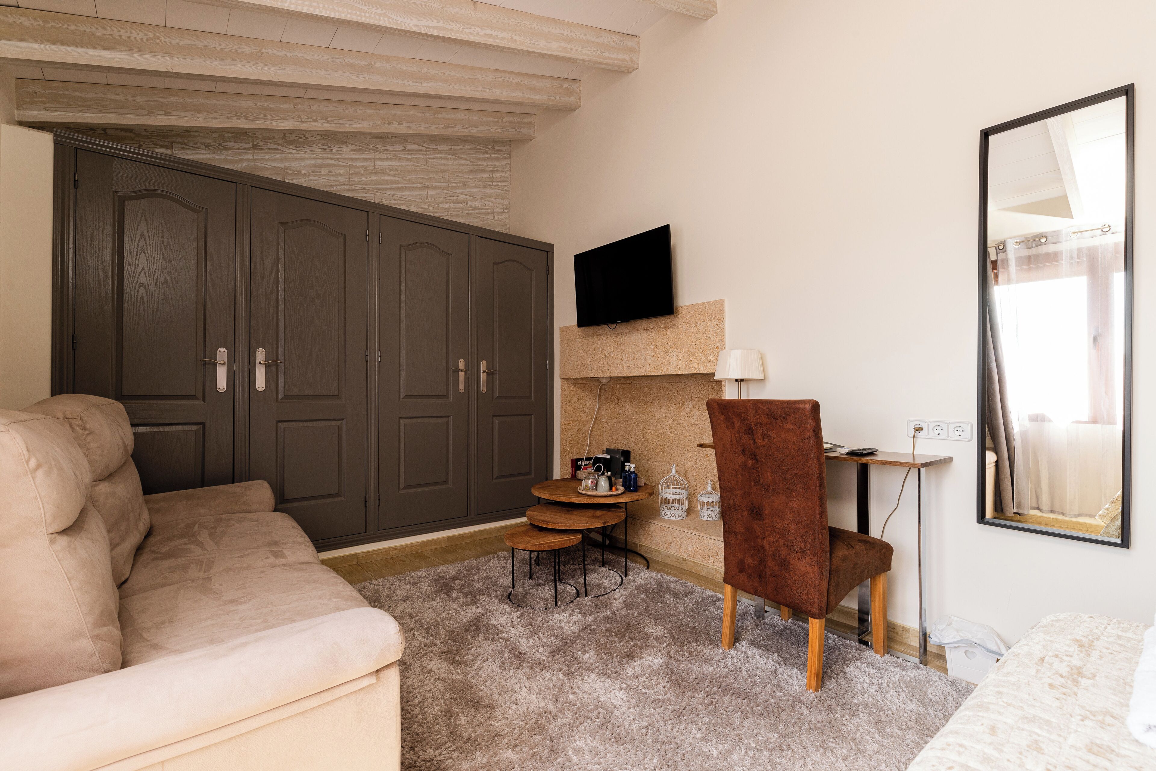 A room with a sofa, a small table with chairs, a TV mounted on the wall, and a wardrobe.