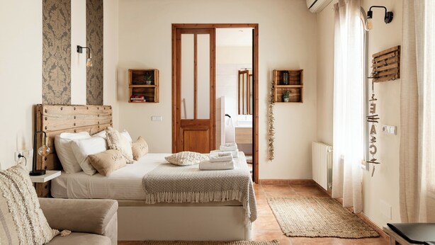 A bedroom with a bed, bedside tables, a wooden headboard, a bedside lamp, a wall-mounted shelf, and a window with curtains. - Casa Mistela (Jalon)